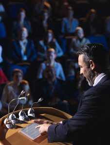High angle view of Caucasian businessman standing and looking at digital tablet on stage in auditorium